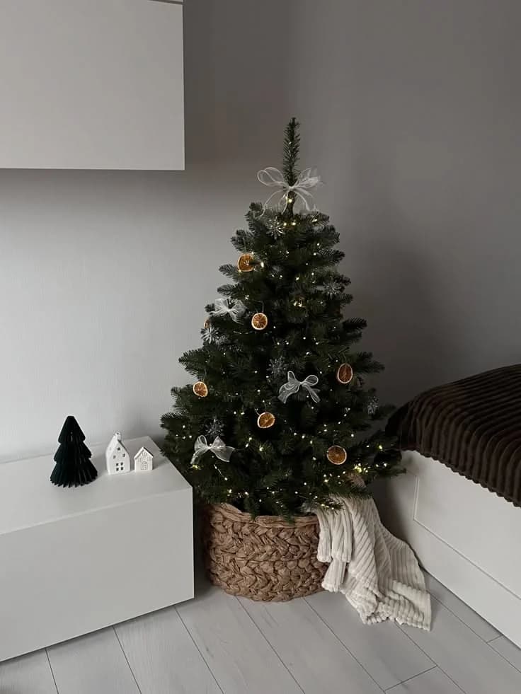 Small tree with dried orange slices and white bows in a braided basket in the corner of a gray bedroom next to a white cabinet
