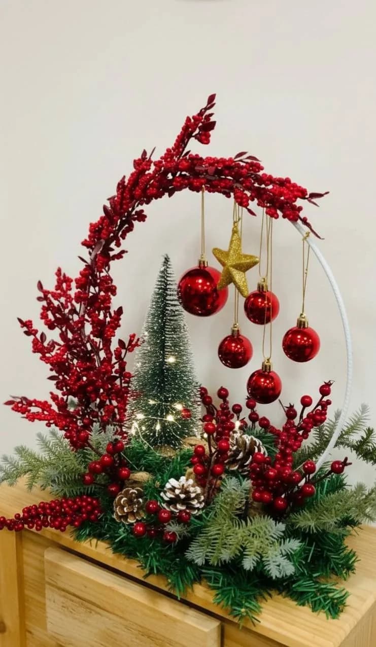 Hoop arrangement half covered in red berry stems with hanging red baubles, a gold star and a mini tree