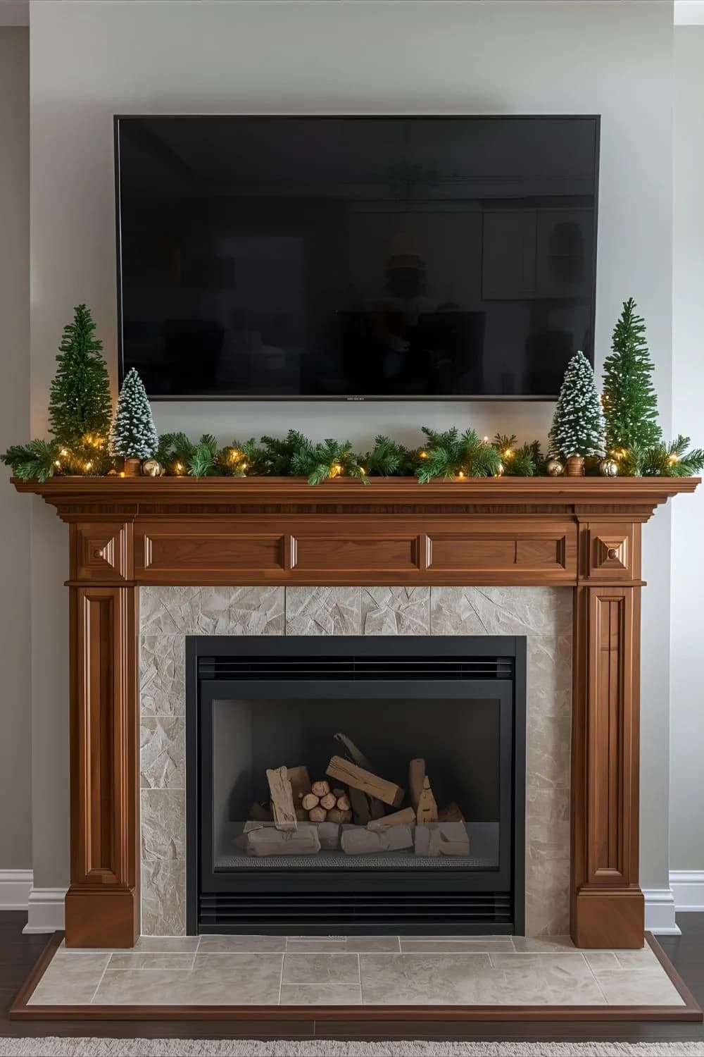 Wooden mantel with a thin lit garland and small trees at both ends under a wall-mounted TV
