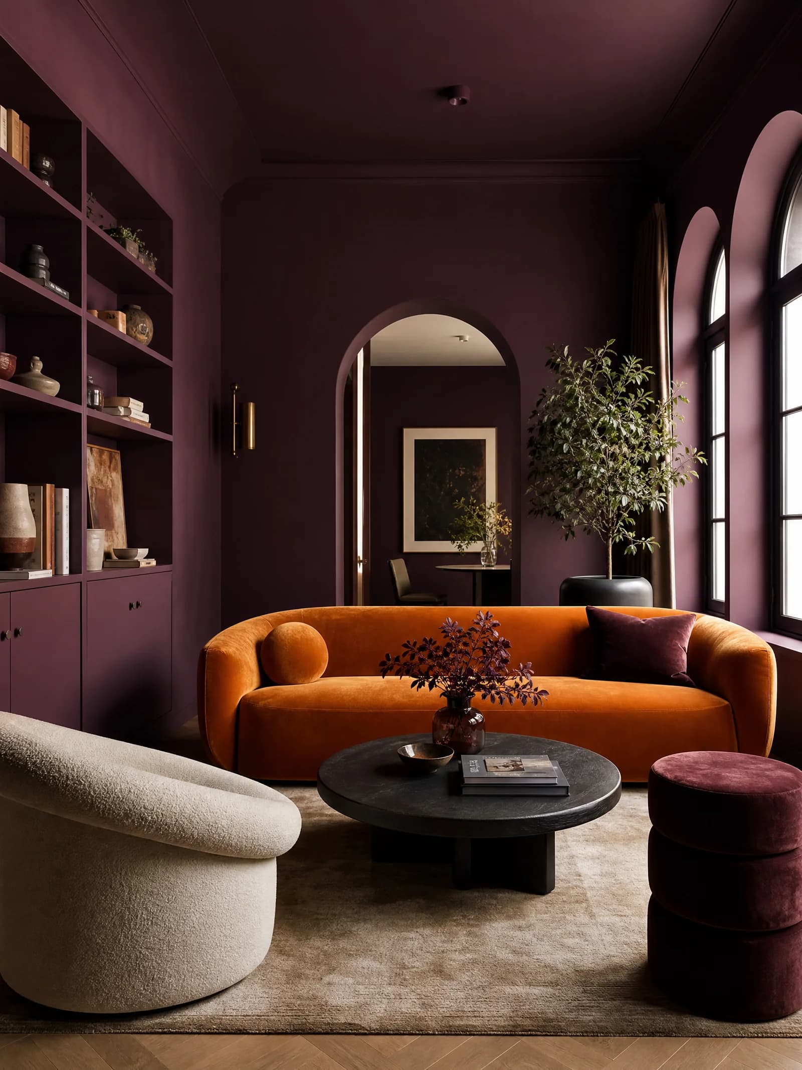 Living room with deep plum walls, ceiling and built-in shelves in one color, an arched doorway, an orange velvet sofa and a cream boucle armchair