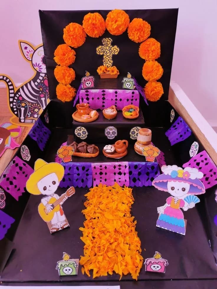 Altar hecho con cajas forradas de negro, arco de flores naranjas de papel, papel picado morado y camino de pétalos de cempasúchil