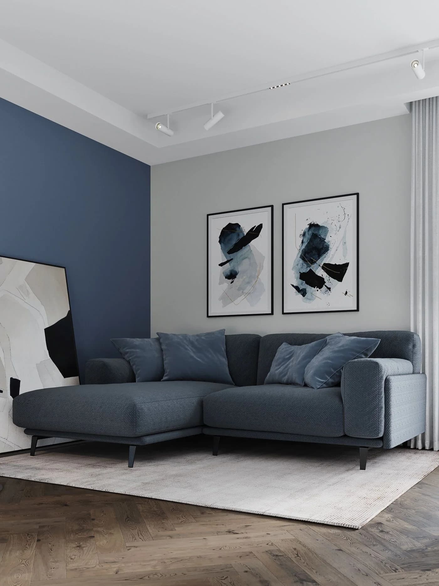 Sala con una pared azul marino y otra gris claro, un sofá esquinero gris azulado con cojines azules, dos cuadros abstractos en azul y negro y un tapete claro