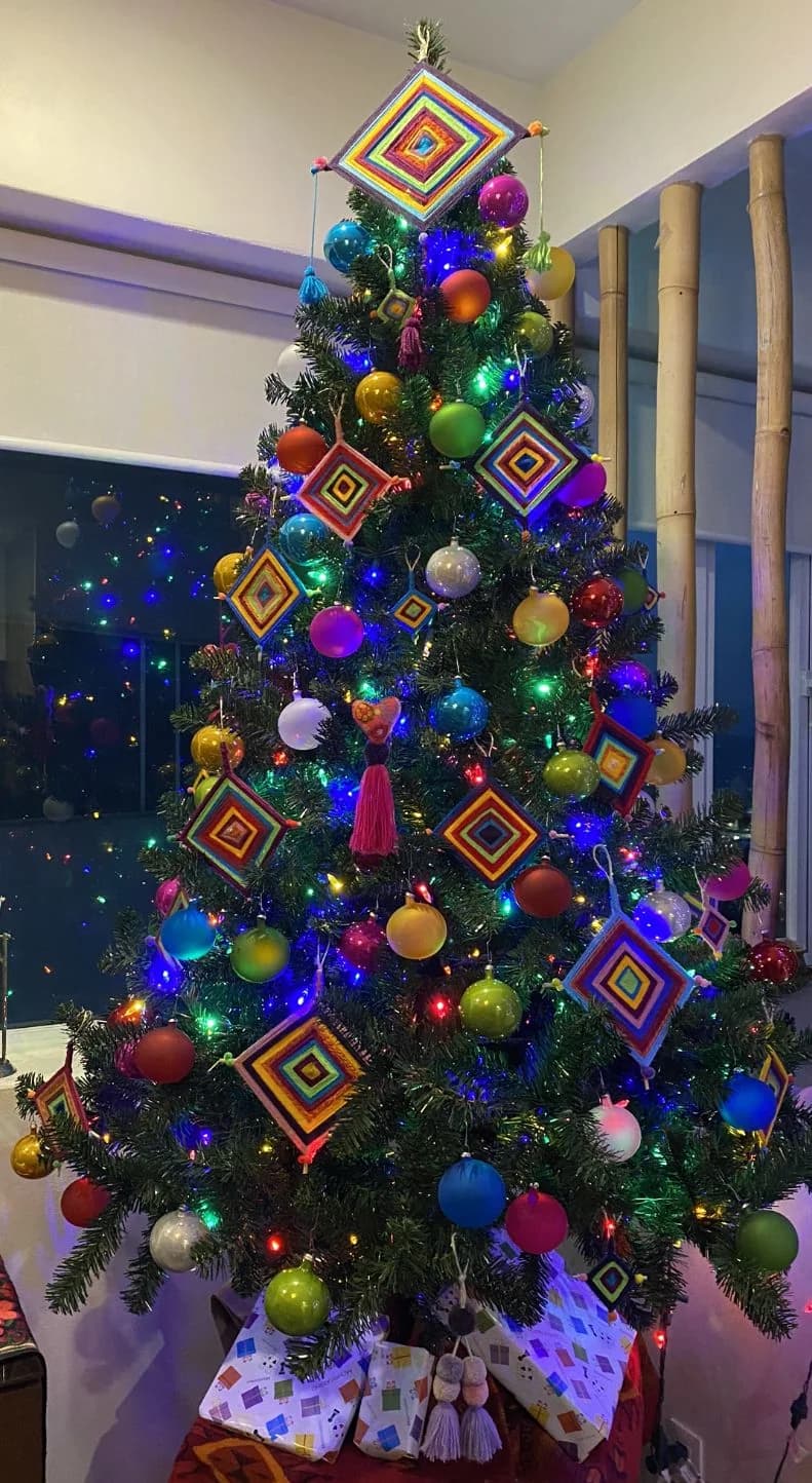 Árbol de Navidad con ojos de dios de estambre de colores, uno grande en la punta, esferas de colores y luces multicolor