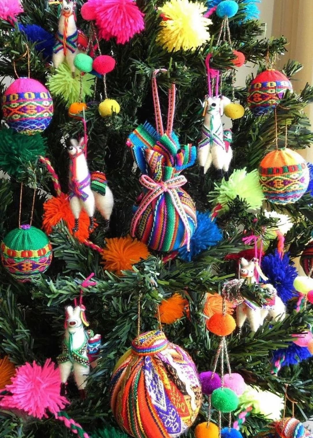 Árbol de Navidad lleno de adornos textiles de colores: esferas bordadas, animalitos de lana, pompones rosas y verdes y bolsitas tejidas