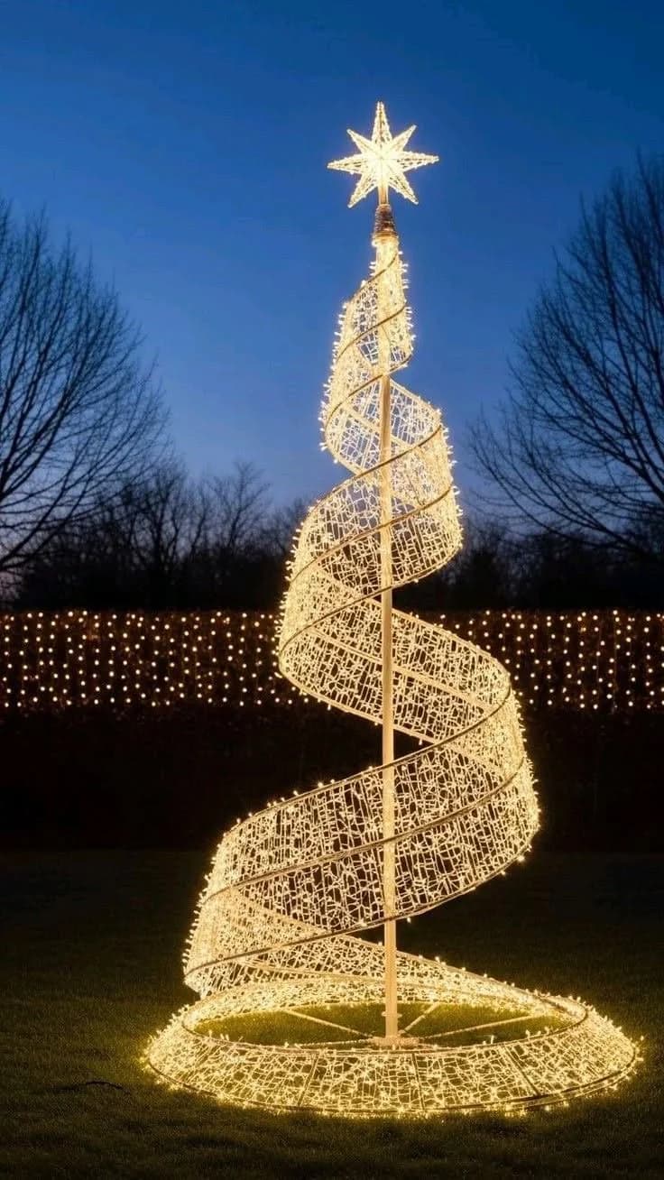Árbol de Navidad en espiral hecho de luces cálidas con una estrella en la punta, sobre el pasto al anochecer