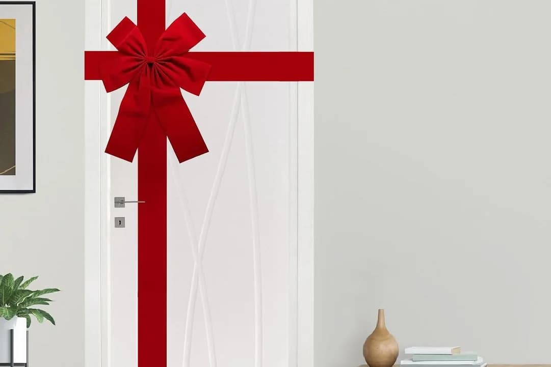 Puerta blanca interior envuelta con listón rojo ancho en cruz y un moño grande, como si fuera un regalo