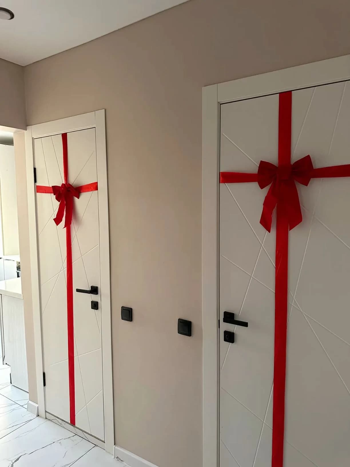 Dos puertas blancas interiores en un pasillo, cada una con un listón rojo en cruz y un moño