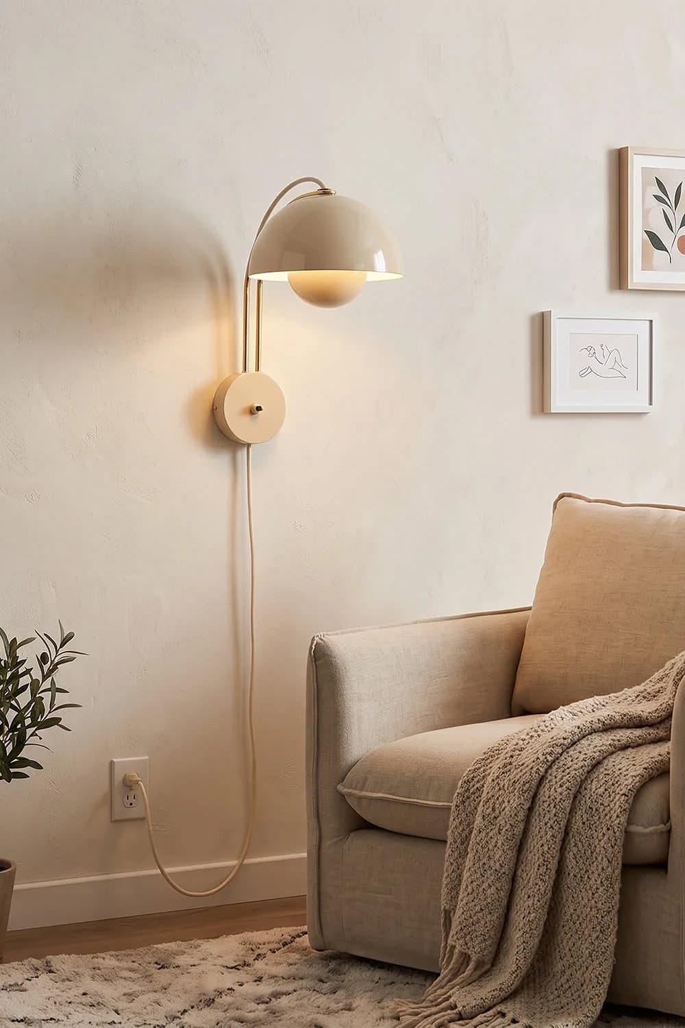 Aplique color crema con pantalla redonda y cable hasta el contacto, junto a un sillón beige con una manta