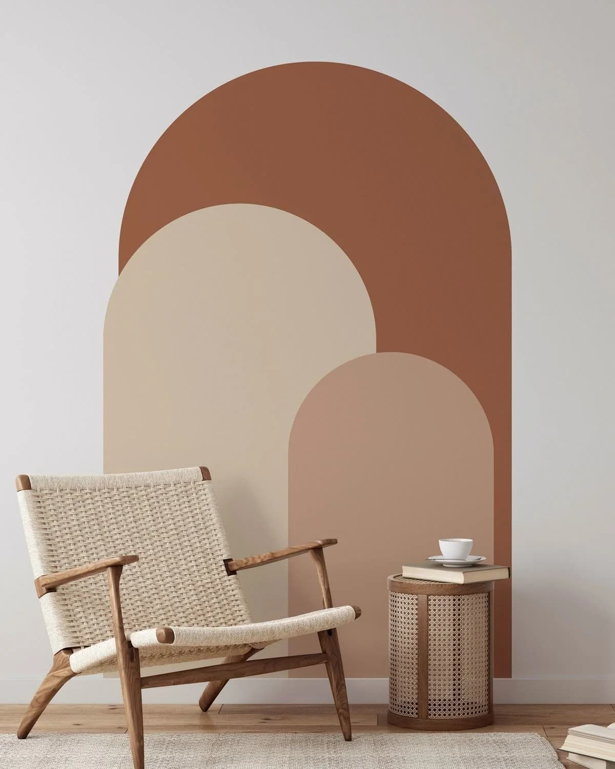 Pared clara con tres arcos pintados encimados en terracota, arena y rosa viejo, con una silla tejida y una mesita de ratán delante