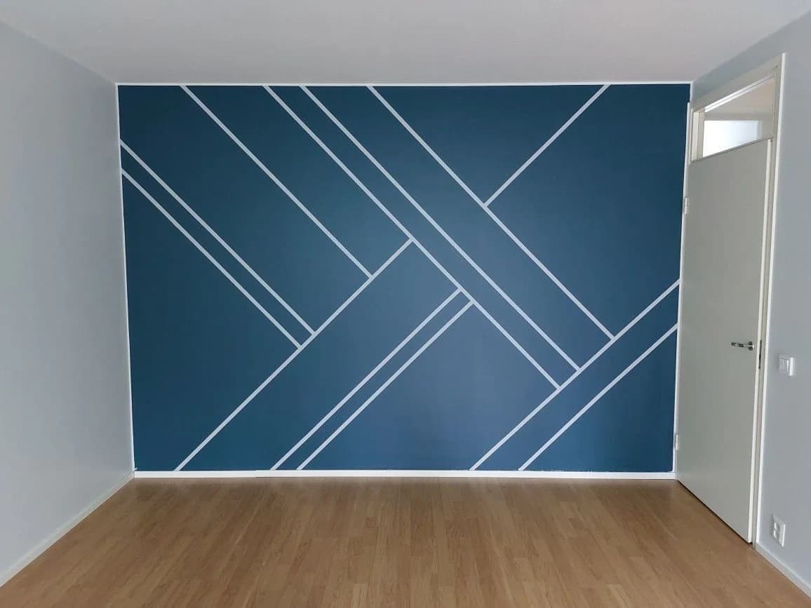 Pared pintada en azul petróleo con líneas blancas delgadas cruzadas en diagonal, en un cuarto vacío con piso de madera
