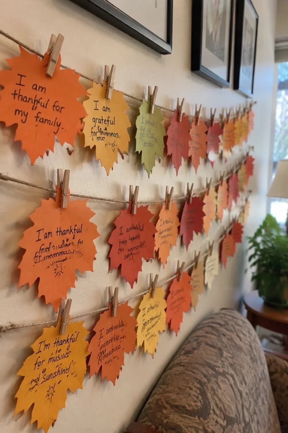 Rows of orange, yellow and red paper leaves with handwritten thankful notes clipped to twine with clothespins on a living room wall