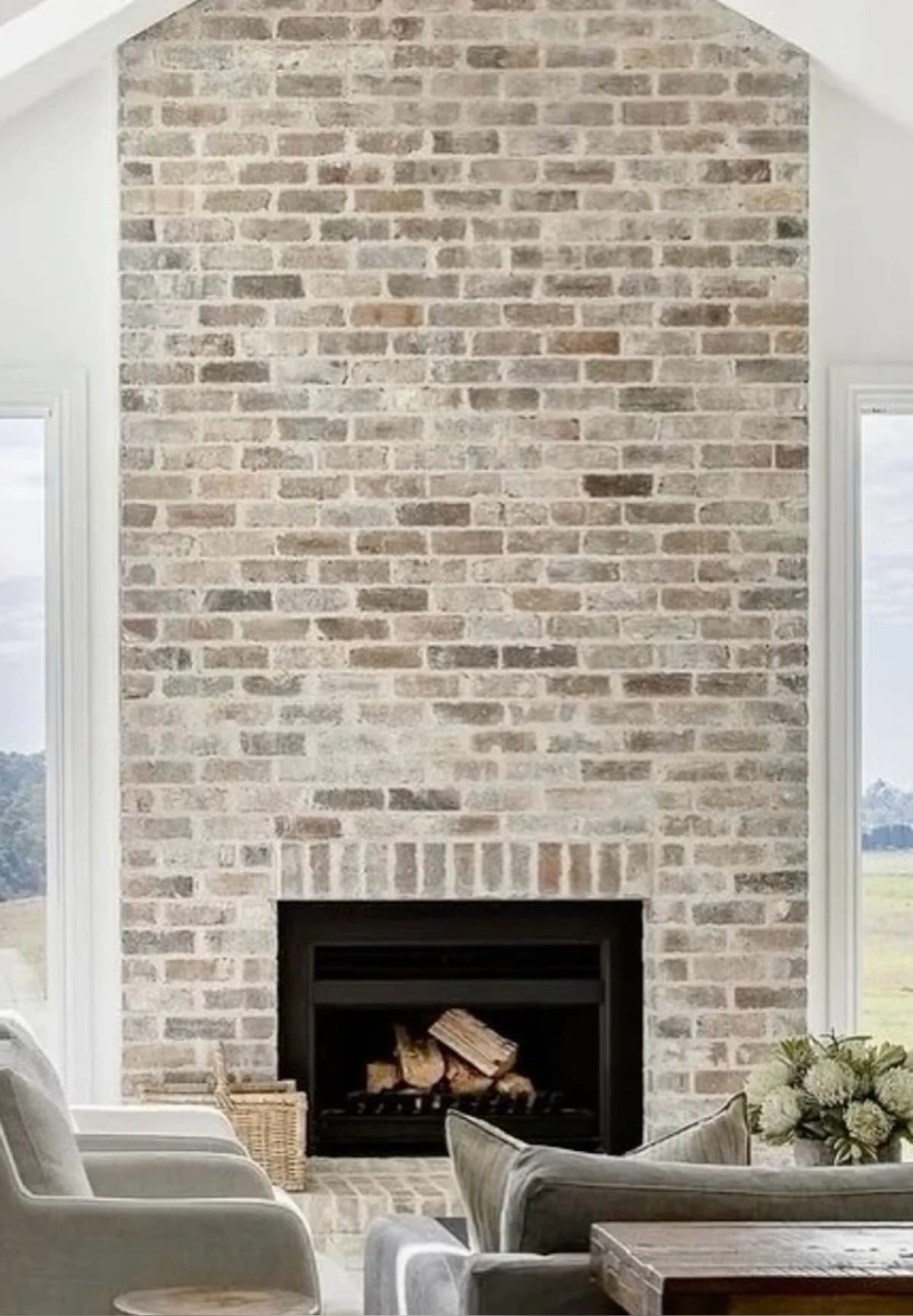 Tall brick chimney breast in a pale, washed finish with the color of individual bricks visible, above a black fireplace insert between two tall windows