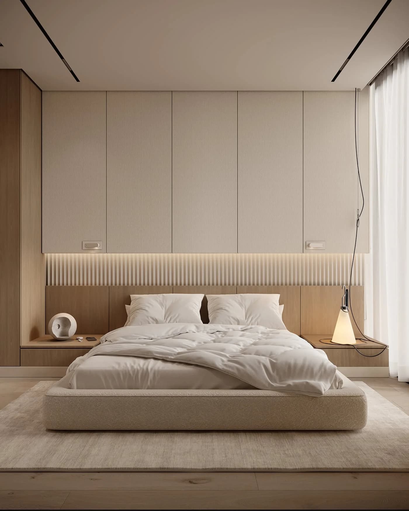 Low upholstered bed with white bedding in front of a wall of flat cream wardrobe doors and a wood ledge with a hidden light strip, with a small cone lamp