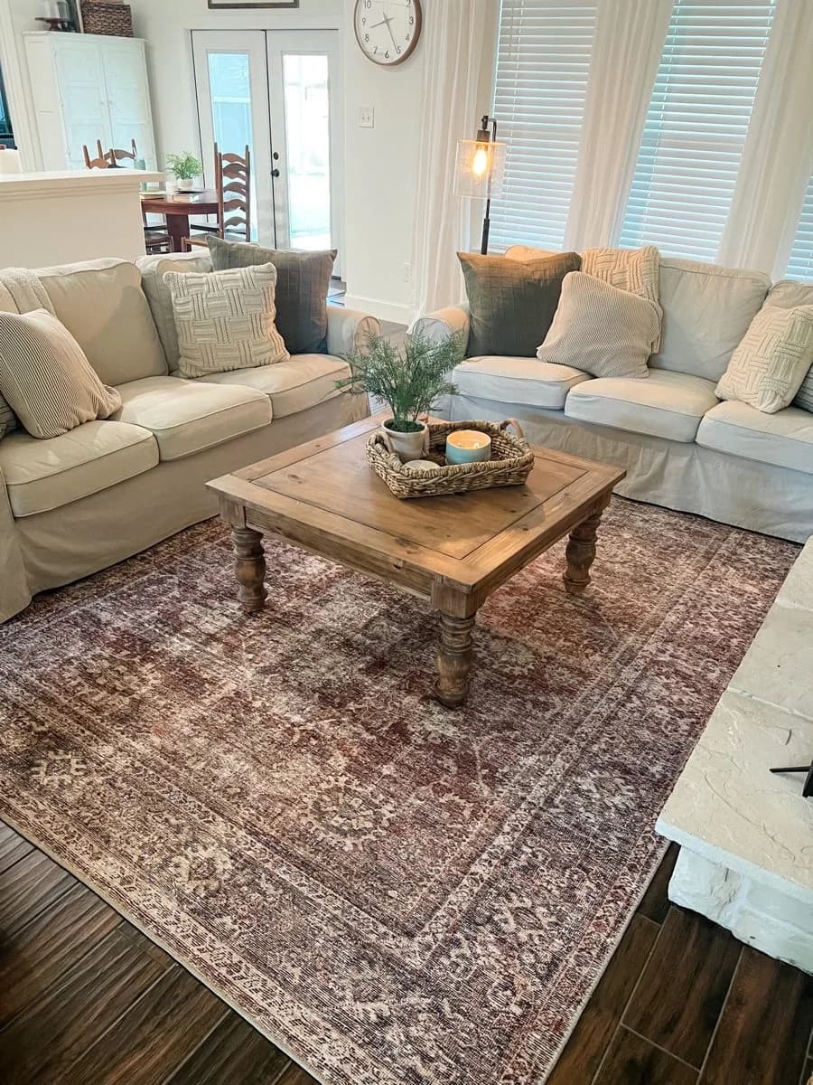 Dark wood floor with a faded rust and plum vintage-style rug under a pale slipcovered sectional and a chunky wooden coffee table